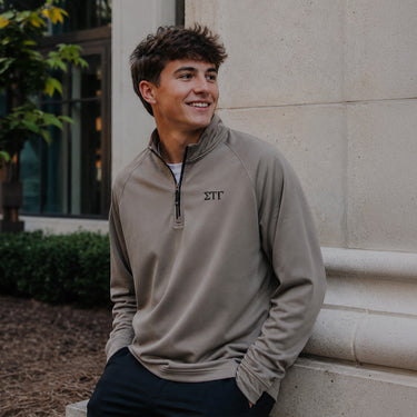 College-aged man wearing the Mushroom Cutter & Buck Adapt quarter-zip with black embroidered Sigma Tau Gamma Greek letters outdoors on campus.
