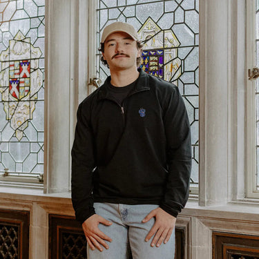 Male model wearing the black Sigma Tau Gamma Embroidered Luxe Quarter Zip in front of stained glass windows with fraternity crests.