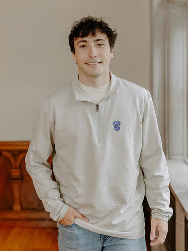 Male model wearing the smoke-colored Sigma Tau Gamma Embroidered Luxe Quarter Zip with crest embroidery, standing by a window in a formal setting.