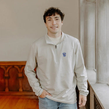 Male model wearing the smoke-colored Sigma Tau Gamma Embroidered Luxe Quarter Zip with crest embroidery, standing by a window in a formal setting.
