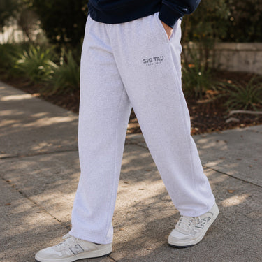 Close-up lifestyle photo of a college-aged male wearing ash gray classic sweatpants with a relaxed straight-leg fit, paired with a navy sweatshirt and white sneakers outdoors.